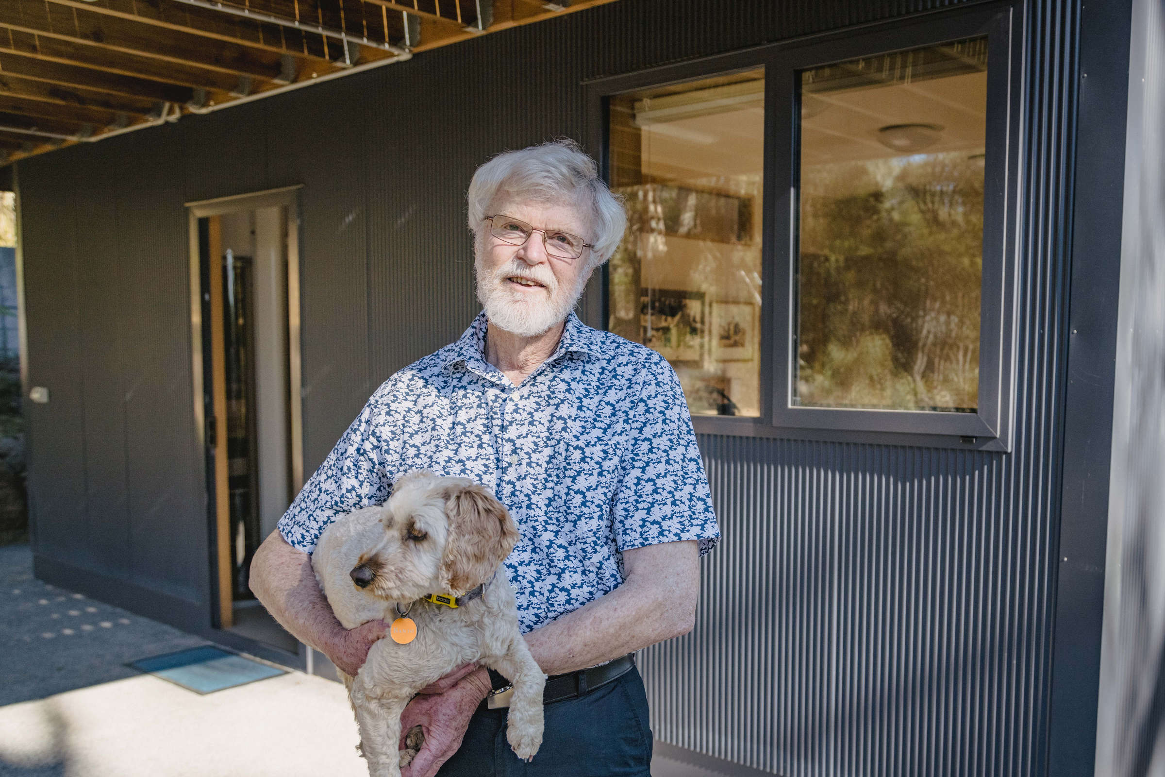 A very happy client holding their cute dog outside the renovated lower level of the house. Externally, the renovation features custom mini orb, double glazed and thermally broken windows and a concrete path exposed aggregate. The renovation was to improve the amenity of the space under the house by building it in, creating two extra bedrooms and a usable under-house storage space. Photo: Jordan Davis.