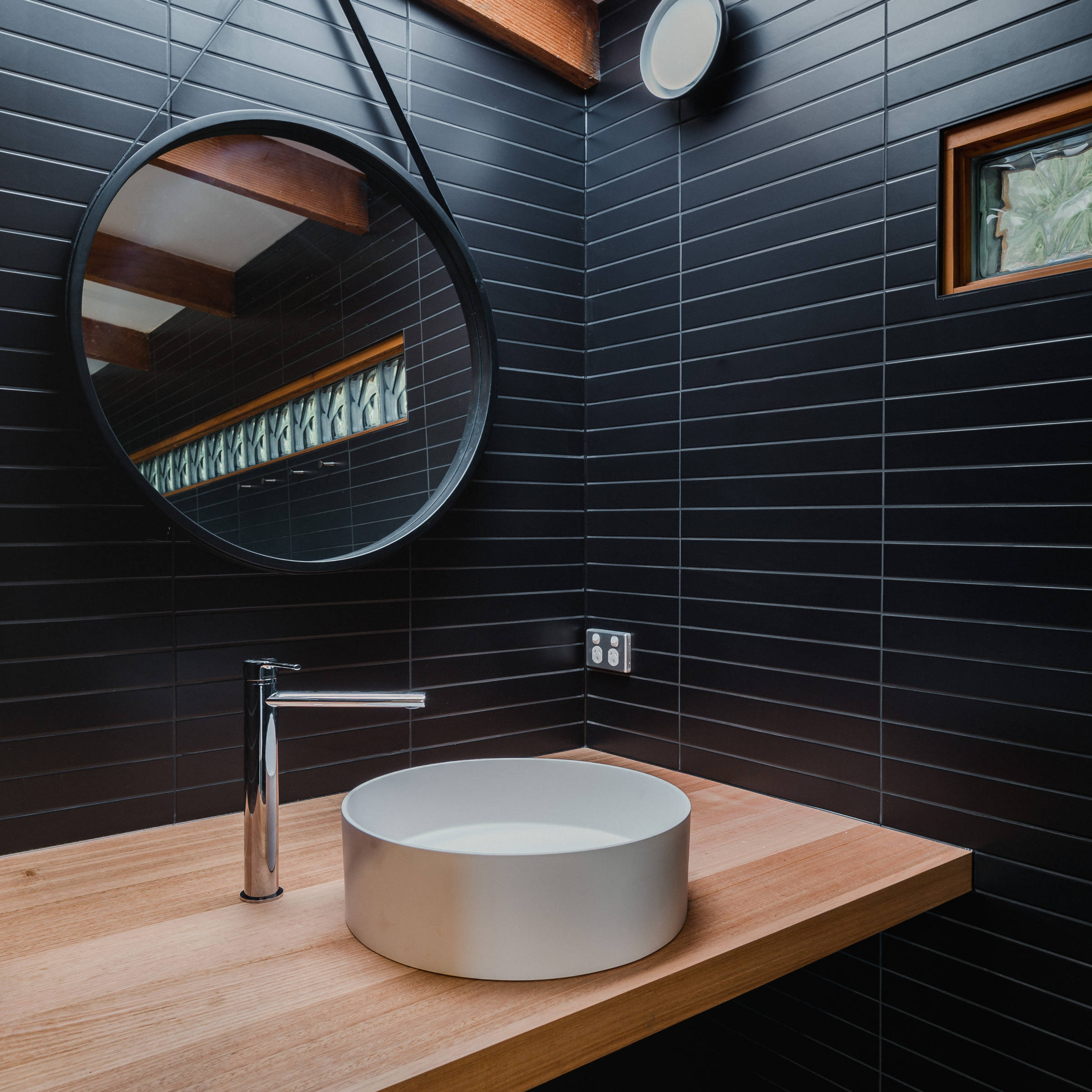 Custom Japanese inspired bathroom renovation featuring black mosaic tiles, hanging mirror, custom timber benchtop in Tasmanian oak. The architectural bathroom renovation was designed to give a contemporary feel and also features a round white basin with increased natural light from a new skylight. Credit: Jordan Davis.