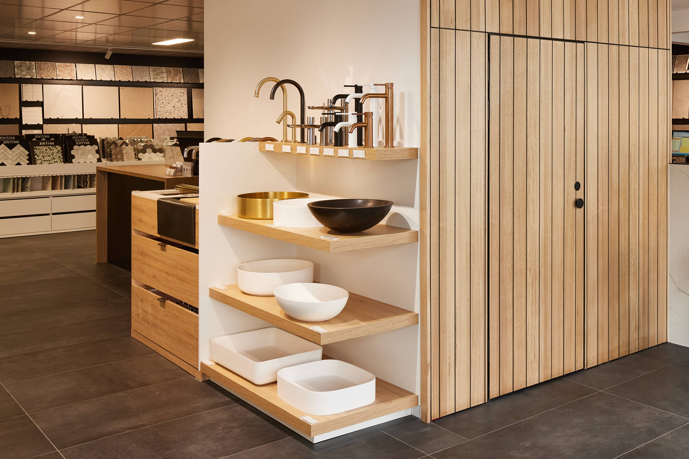 An aspect of the Rossetto Tiles showroom, featuring four timber shelves displaying taps and bathroom basins. The image details neat Tasmanian oak timber panelling for an internal room and the area is bright and well lit. Credit: Samuel Shelley.